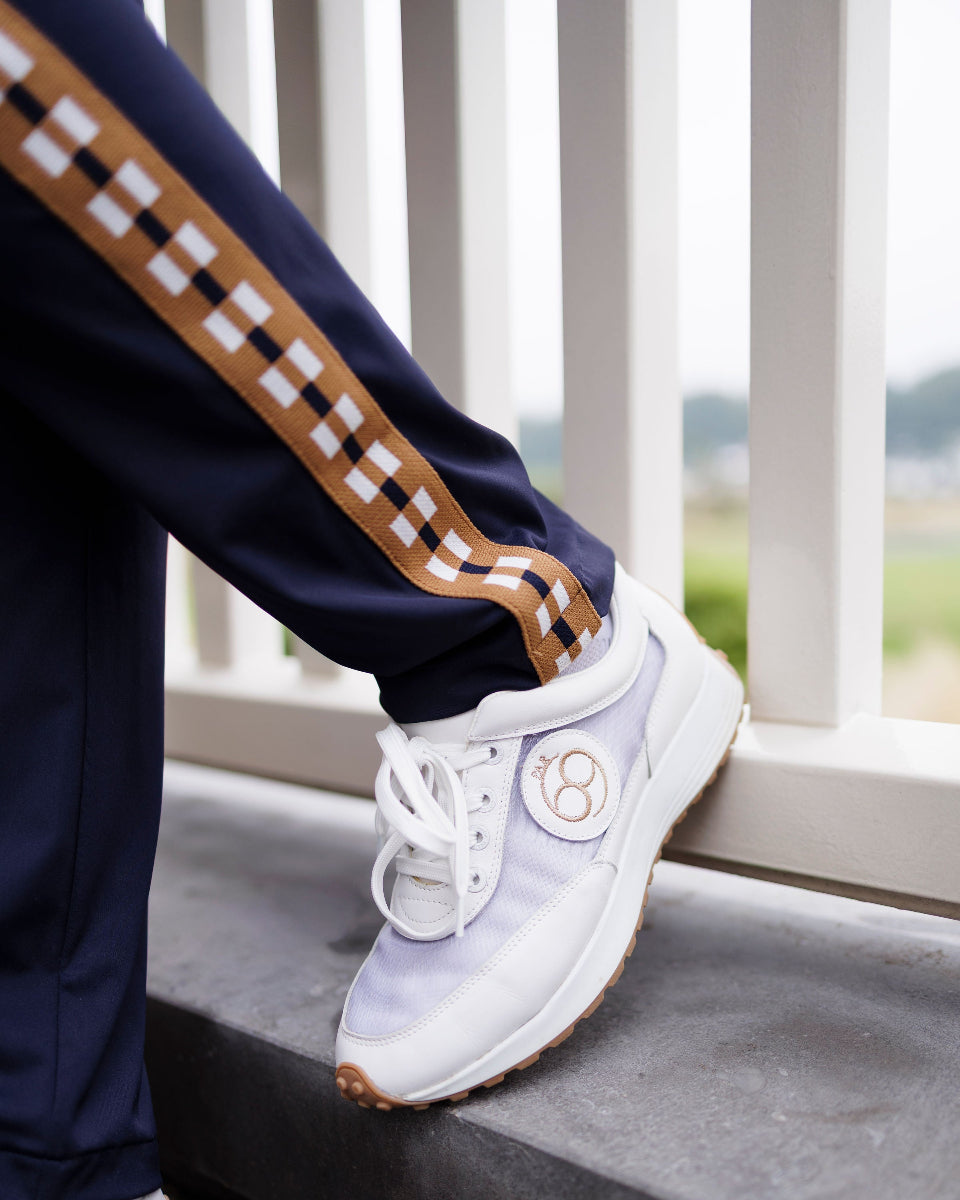 Person wearing white sneakers with a brand logo, standing on a concrete ledge with a scenic background.