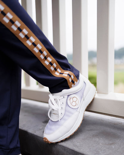 Person wearing white sneakers with a brand logo, standing on a concrete ledge with a scenic background.